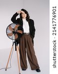 Small photo of Fashion studio photo of stylish European brunette woman in in long baggy pants and a black jacket posing on white background. Trendy office style in clothes.
