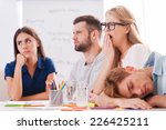 Boring presentation. Group of young business people in smart casual wear looking bored while sitting together at the table and looking away 