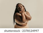 Small photo of Beautiful voluptuous African woman in underwear touching face and smiling on studio background
