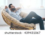 Total relaxation. Handsome young man keeping eyes closed and holding hands behind head while sitting in big comfortable chair at home  