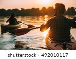 Meeting sunset on kayaks. Rear view of young couple kayaking on lake together with sunset in the backgrounds