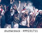 Christmas fun. Group of beautiful young people in Santa hats throwing colorful confetti and looking happy