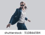 Style in motion. Handsome young man in full suit and sunglasses moving in front of grey background