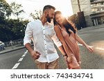 Her happiness is everything to him. Beautiful young couple holding hands and smiling while walking through the city street