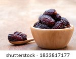 The large date fruits (Medjool) in cups and wooden spoons on a cement with blurred background.