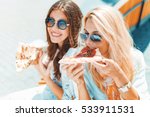 Portrait of two young women eating pizza outdoors,having fun together.