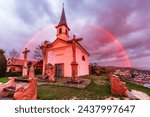Small photo of The Chapel of Saint Thomas Becket in Szent Tamas lighten by a strong sunlight with a rainbow behind in rainy clouds in Esztergom, Hungary.
