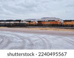 Small photo of Gillette, Wyoming - Janaury 23, 2021: Road next to a railroad track with train engines on a cold, snowy cloudy winter day in Gillette, Wyoming.