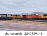 Small photo of Gillette, Wyoming - January 23, 2021: Trains on a track next to a road with hills in the background on a cloudy winter day near Gillette, Wyoming.