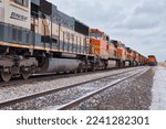 Small photo of Gillette, Wyoming - January 23, 2021: Two train track with train engines next to a small road on a cloudy winter day near Gillette, Wyoming.