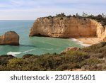 Limestone rock cliffs and rock in the Atlantic Ocean with a small sandy beach on a sunny winter day along the Seven Hanging Valleys Trail in southern Portugal.
