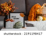 Small photo of Cozy autumn concept. Home warmth in cold weather. Still-life. A blanket, pumpkins, flowers and the inscription home on the coffee table in the home interior of the living room.