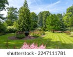 In this carefully mowed lawn is a large vase, surrounded by Astilbe and various types of trees and shrubs in an arboretum in Rotterdam, Netherlands