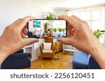 Augmented reality concept: hands holding smart phone with AR interior decoration app, visualising the living room with added poster and pillow print.