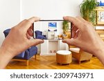 Augmented reality concept: hands holding smart phone with AR interior decoration app, visualising the living room with additional photo frame.