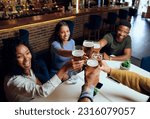 Happy young multiracial group of friends in casual clothing toasting with beers at restaurant