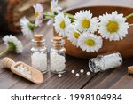 Bottles of homeopathy granules. Homeopathic remedy - Chamomilla. Daisies flowers in wooden bowl. Homeopathy medicine concept. 