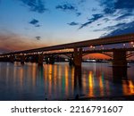 Two bridges: metro subway bridge and arched October road bridge over the Ob River in the big city Novosibirsk at night with reflections of lantern lights, Novosibirsk, Siberia, Russia- 22.09.2022: