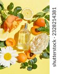 Small photo of Open bottle of perfume with roses, green leaves, apricot, lemon, chamomile, drops of water on the yellow background. Fresh aroma. Idea of sweet pure smell for young girls. Fruity and flowery perfume