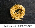 Small photo of One Single Tagliatelle Pasta Nest on a Dark Background: A pasta nest of dried noodles viewed closeup from directly above