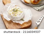 Oven baked camembert cheese with lye baguette bread on wooden board, grey concrete surface. Homemade grilled brie with thyme, rustic style table setting