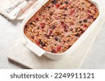 Small photo of breakfast casserole idea - oven berry baked oatmeal with almonds, walnuts and coconut flakes in a white porcelain baking form on a marble board, top view