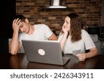 Small photo of Married couple sits in kitchen at a laptop and analyzes their finances and debts. Man is shocked by his wife's excessive spending, looking at the check.Financial literacy, irrational spending of funds