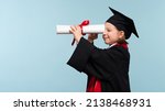 Small photo of Funny Whizz kid girl wearing graduation cap and ceremony robe on light blue background. Graduate celebrating graduation. Education Concept. Smart child looks to the future through the certificate