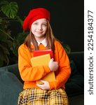 Small photo of Smile schoolgirl holds two books. Girl wears bright outfit and woolen red beret. Concept of bookworm, bibliophile and International Children's Book Day