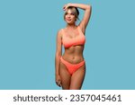 Slim woman posing in an orange swimsuit on a blue background. Healthy slender girl shows epilation or depilation of armpits, smooth healthy skin without damage and irritation 