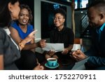 Young African businesspeople laughing together while going over paperwork during a casual meeting in an office