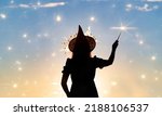 Small photo of Black silhouette of witch with magic wand isolated on fairy star sky background.Beautiful young woman in black robe and wizard hat conjuring, making witchcraft. Halloween party art design.Copy space