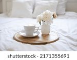 Light cozy bedroom, Coffee or tea cup and an flowers on the white bed. Breakfast in bed. Coffee cup and flowers on a white bed. White Concept.