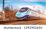 Small photo of Modern high speed aerodynamic streamlined electric train on rail during sunset passing by with motion blur.