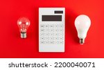 Small photo of White calculator and incandescent lamp or LED bulb on red background. Concept showing the payment of electricity bills. The concept of savings electricity. Reducing the payment of utility bills.