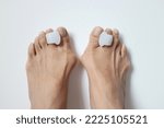 Small photo of Soft defocused photo of a pair of bunion feet wearing toe separators closed up on off white background