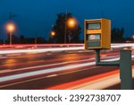 A radar-equipped speed camera monitors the traffic on a road, flashing a yellow light when it catches a car exceeding the speed limit, and using technology to identify the vehicle and enforce the law.