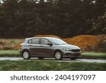 Small photo of Car speeding in the countryside. Driving fast on a road surrounded by greenery in a modern hatchback. Side view of modern hatchback moving on the highway.
