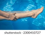Small photo of Close up of woman having cramp on her legs after swimming in swimming pool. To relieve muscle cramps during swimming, stretch, and massage cramped muscles and the surrounding area.