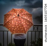 Small photo of Amazing photo of rainy season of monsoons, wherein an unrecognizable teenage girl is holding a peach colored umbrella with polka dots design, while standing on a cliff edge, enjoying the clouds.