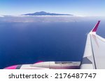Window view from an airplane on the volcano mountain peak of Pico del Teide on Tenerife, Canary Islands, Spain, Europe, EU. High peak are shrouded in clouds. Flying high above the ground. Freedom