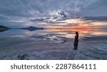 Silhouette of woman walking into the sunset of lake Bonneville Salt Flats, Wendover, Western Utah, USA, America. Beautiful summits of Silver Island Mountain range reflecting in water surface. Awe