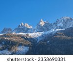 Scenic view of white snowcapped mountain peaks in Charmonix, French Alps, France, Europe. Snowy summits and dark green coniferous trees hill and blue winter sky. Chamonix Needles chain near Mont Blanc