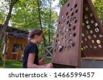 Small photo of Tarusa, Russia - June 1, 2019: An attractive girl in a black T-shirt plays an interesting game in which you need to deliver the ball with the help of two ropes to the top hole in the wooden panel