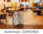Small photo of Tip jar in restaurant dining room. Service industry tipping, minimum wage and gratuity concept.