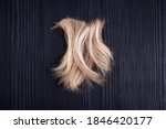 Small photo of Blond wavy hair lock black wooden background close up, cut off natural blonde hair curl on dark wood, haircut, hairstyle, human hair clipping, hair snip, shearing, hairdo, coiffure, barber, copy space