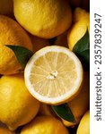 Small photo of Top view picture of many lemons filling the shot. High contrast vibrant yellow color. Beautiful texture of the citrus. One lemon is sliced and has leaves around it.