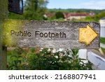 Weathered public footpath sign featuring a yellow arrow indicating a public right of way in a rural location