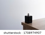 Small photo of Dicey dark black perfume bottle on the edge of wooden table in empty room. Essence without a cap. Clean and minimal picture style.