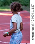 Small photo of Rear view of a African American girl holding a basketball on the court, poised to play, capturing a moment of anticipation and sportsmanship, sports activities from a young age. High quality photo